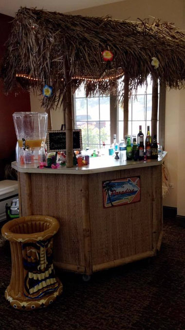Wooden tiki bar with thatched roof, drinks, and a matching stool.