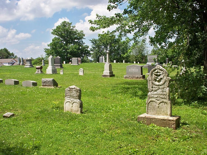Varied old gravestones scattered across a green, sunlit rural Cemetery.