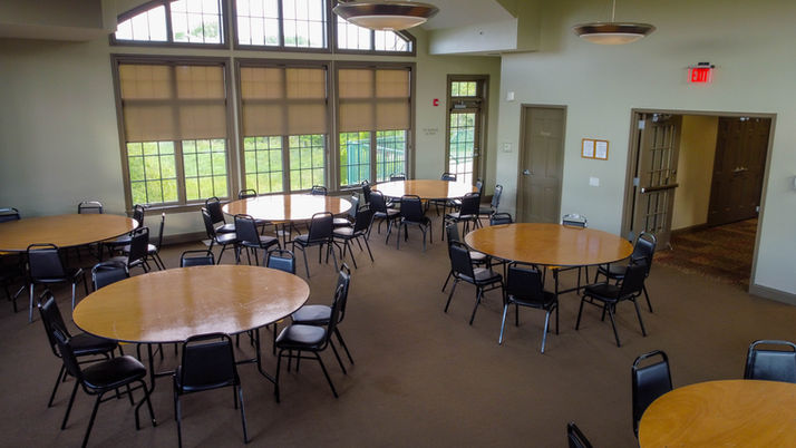 Empty room with many round tables and chairs near large windows.