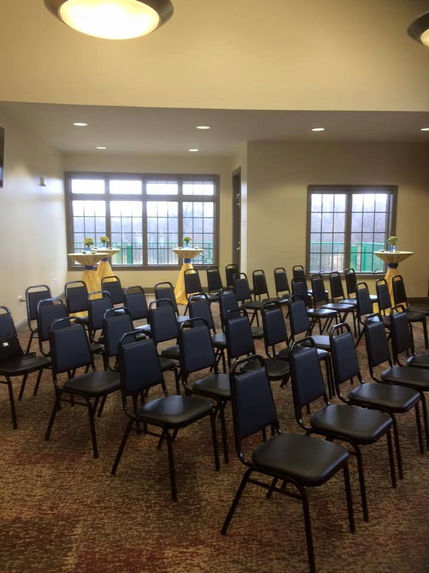 Empty dark blue chairs in rows facing two podiums, windows in background.