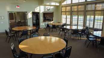 Spacious empty room with many round tables and black chairs.