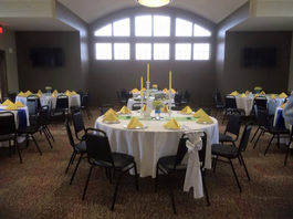 Elegant event room with round tables, yellow napkins, and arched window.