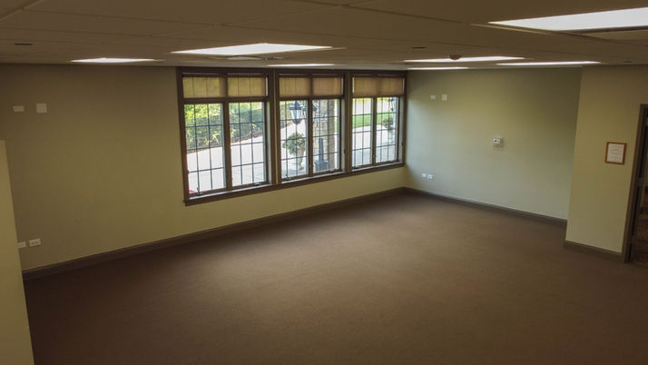 Empty room with brown carpet, light walls, and three large windows.